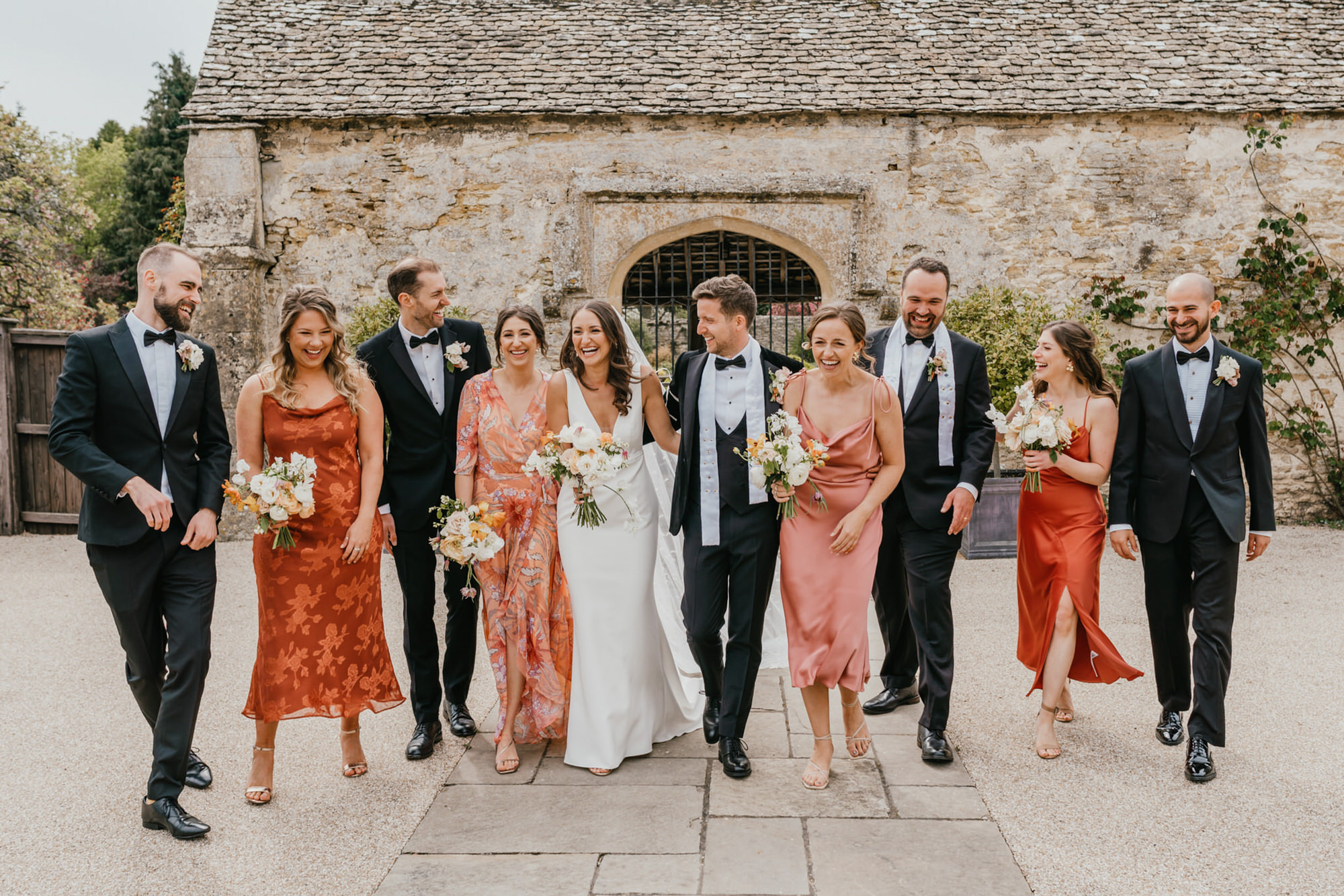 bridal party walking and laughing in front of the loggia at caswell house wedding venue in oxfordshire