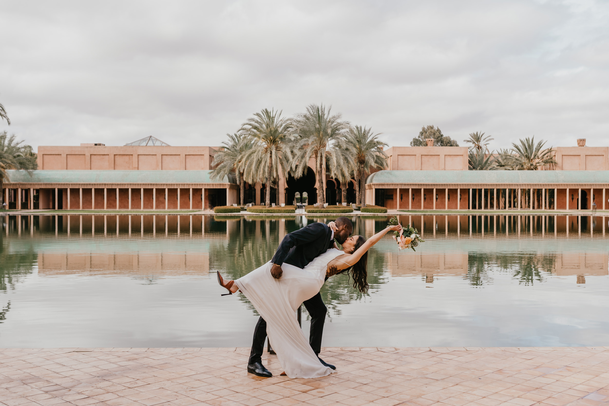 bride and groom dip-kiss in front of the pool at amanjena marrakech wedding venue