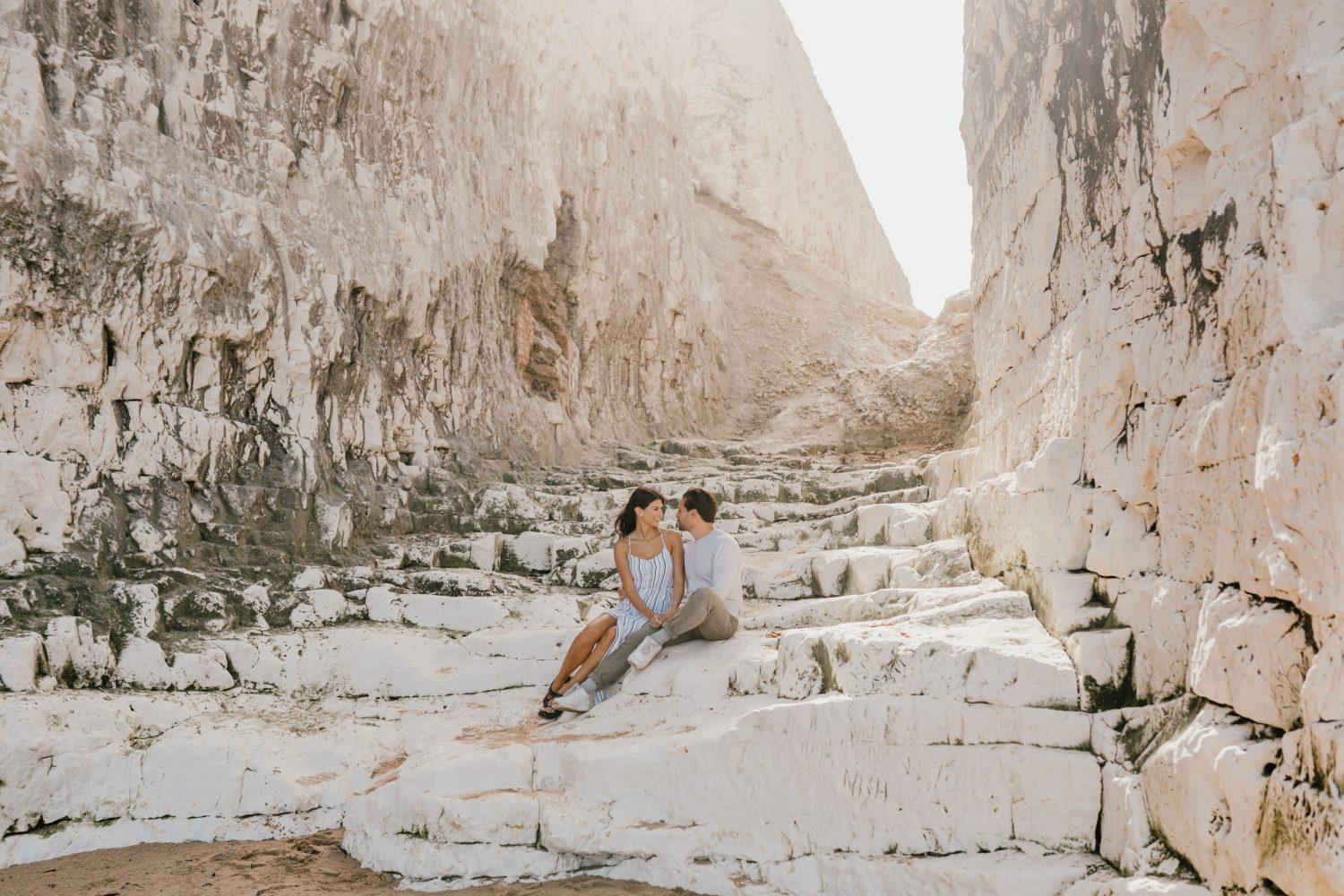 couple sat together on chalk steps at the beach with soft sunlight behind them