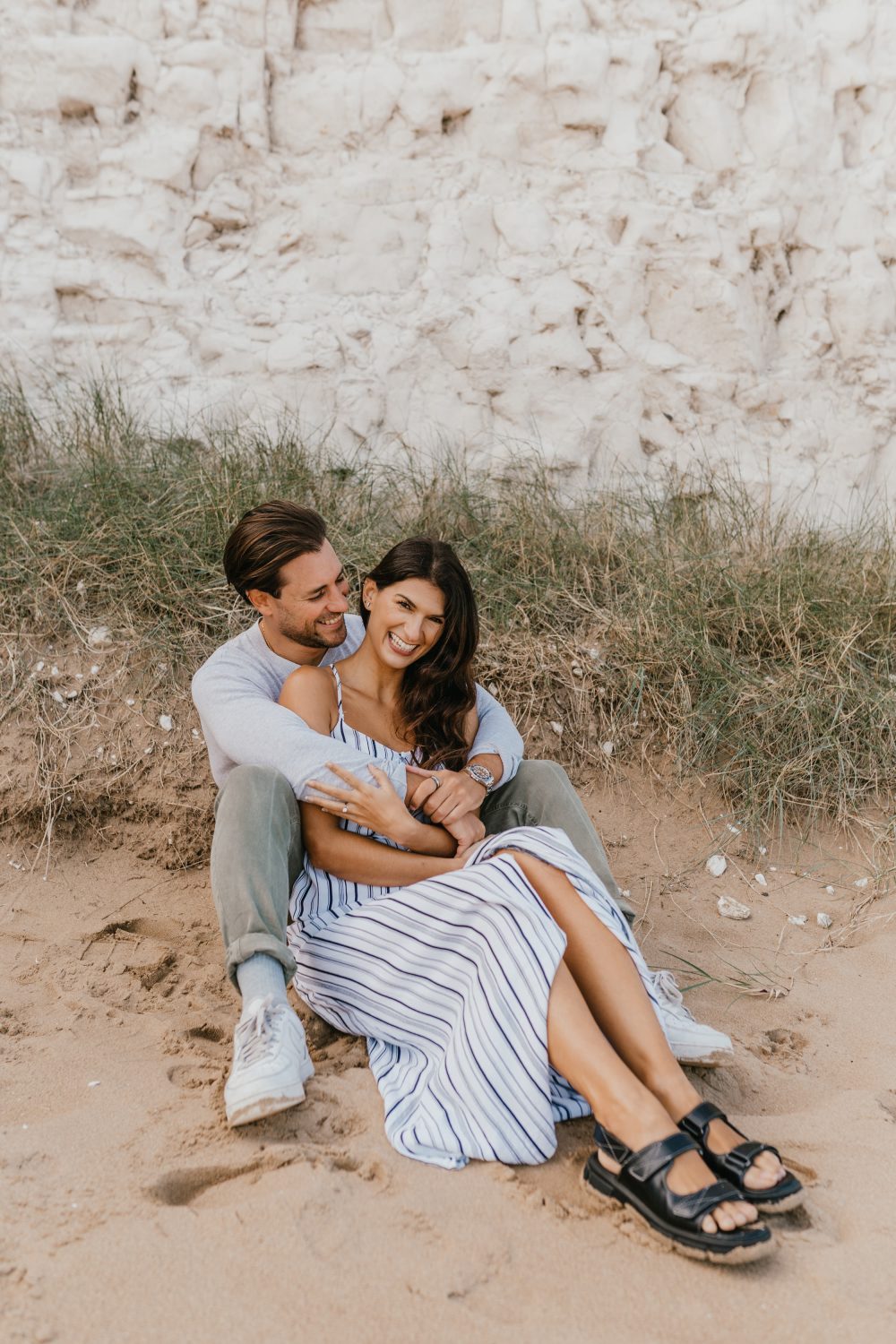 couple sit together laughing on a sandy beach