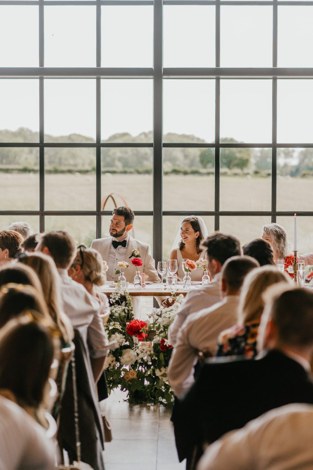 bride and groom sat at the top table in front of the glass wall of the main barn at botley hill