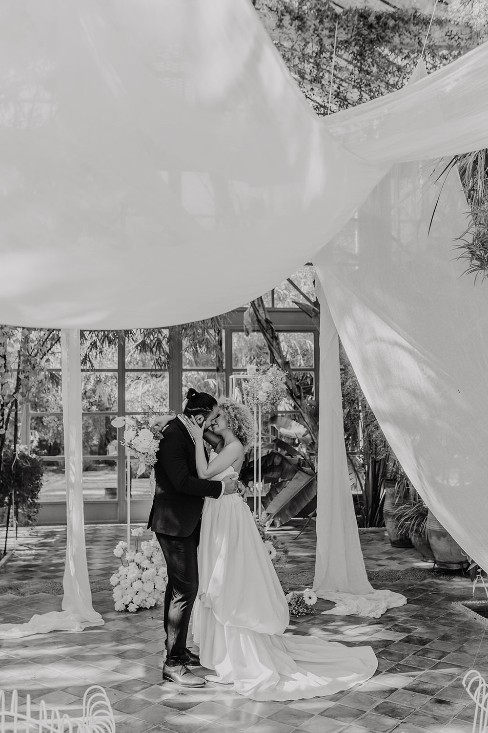black and white photo as bride and groom kiss at the altar at beldi club glasshouse wedding ceremony