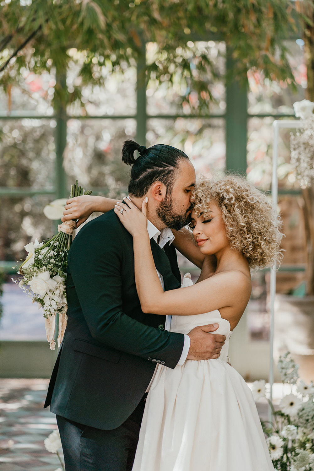 groom kisses bride's forehead in the glasshouse at beldi country club wedding ceremony