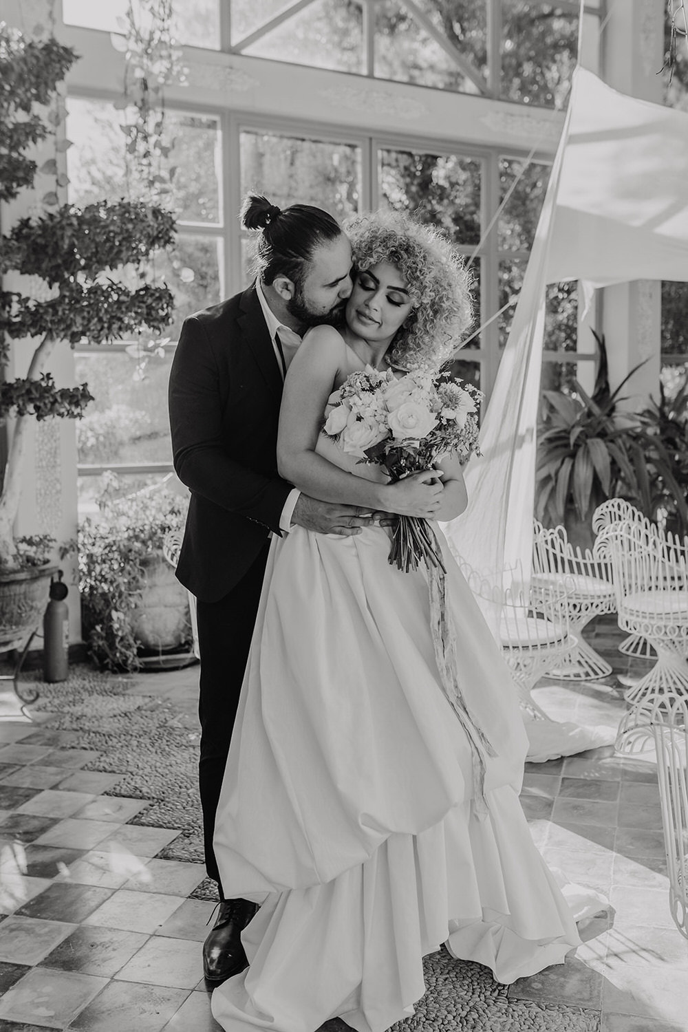 black and white photo as bride and groom embrace in golden hour light in the greenhouse at beldi country club in marrakech