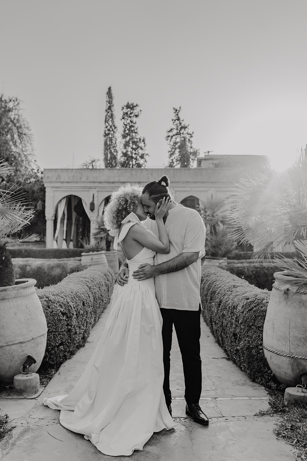 black and white photo of bride and groom kissing in the gardens in golden hour light at beldi country club wedding venue in marrakech
