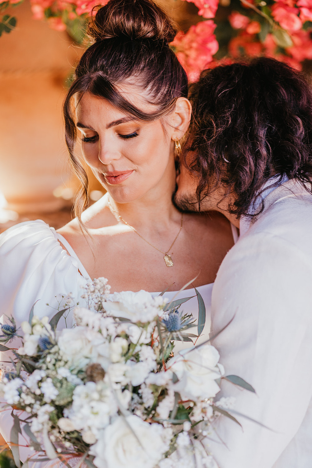 groom kisses bride's neck as she looks at her bouquet at marrakech wedding venue beldi country club