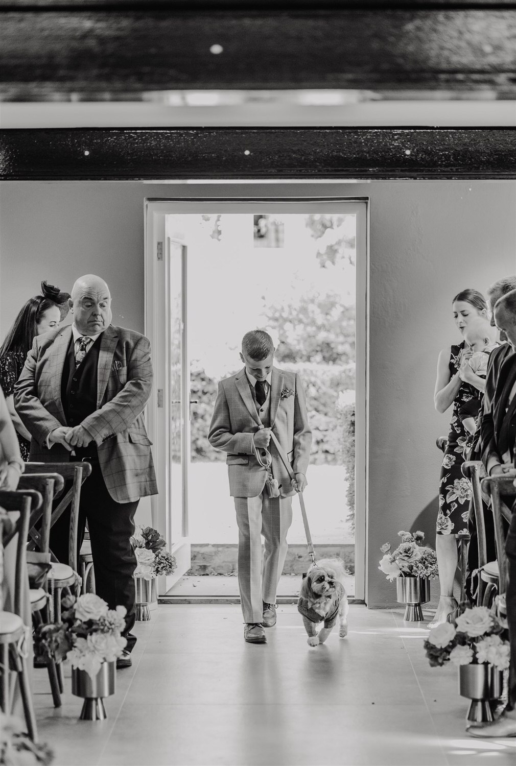 black and white photo of groomsman walking down the aisle with dog at chapel house estate wedding