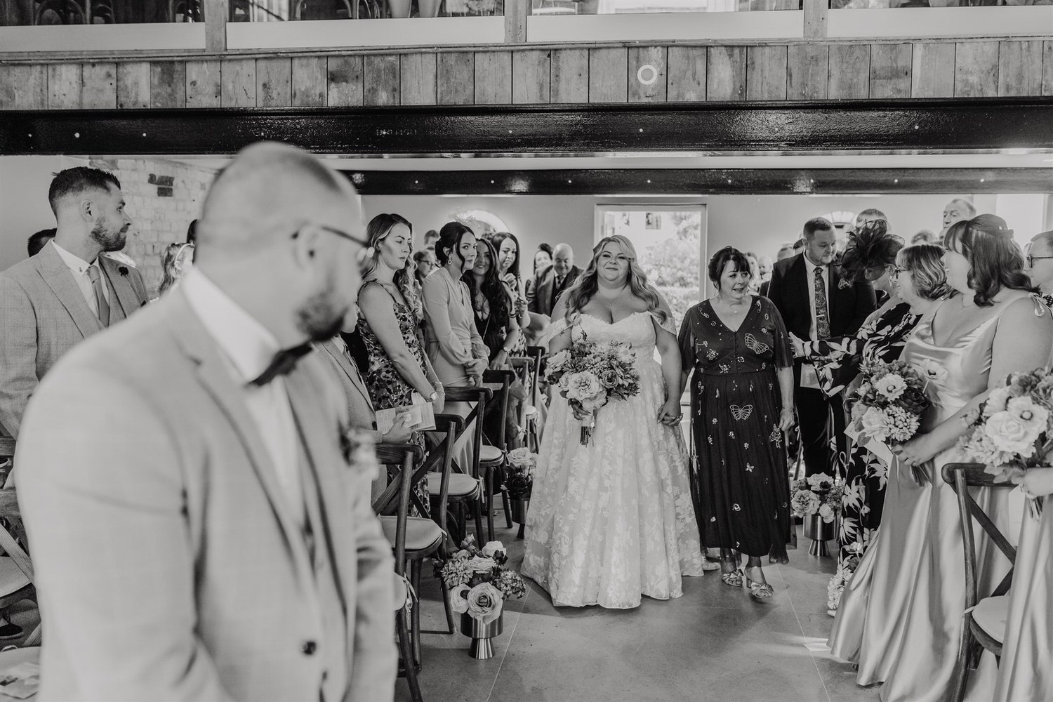 black and white photo of groom watching bride walking down the aisle with her mum at chapel house estate wedding