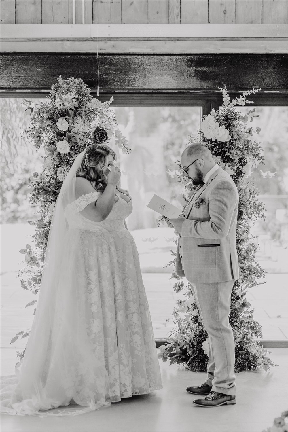 black and white photo of groom reading his vows as bride looks at him at indoor ceremony at chapel house estate in kent