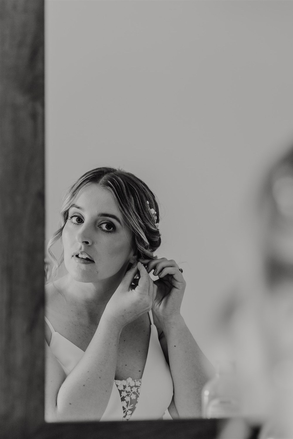 black and white photo of bride putting in her earrings in mirror