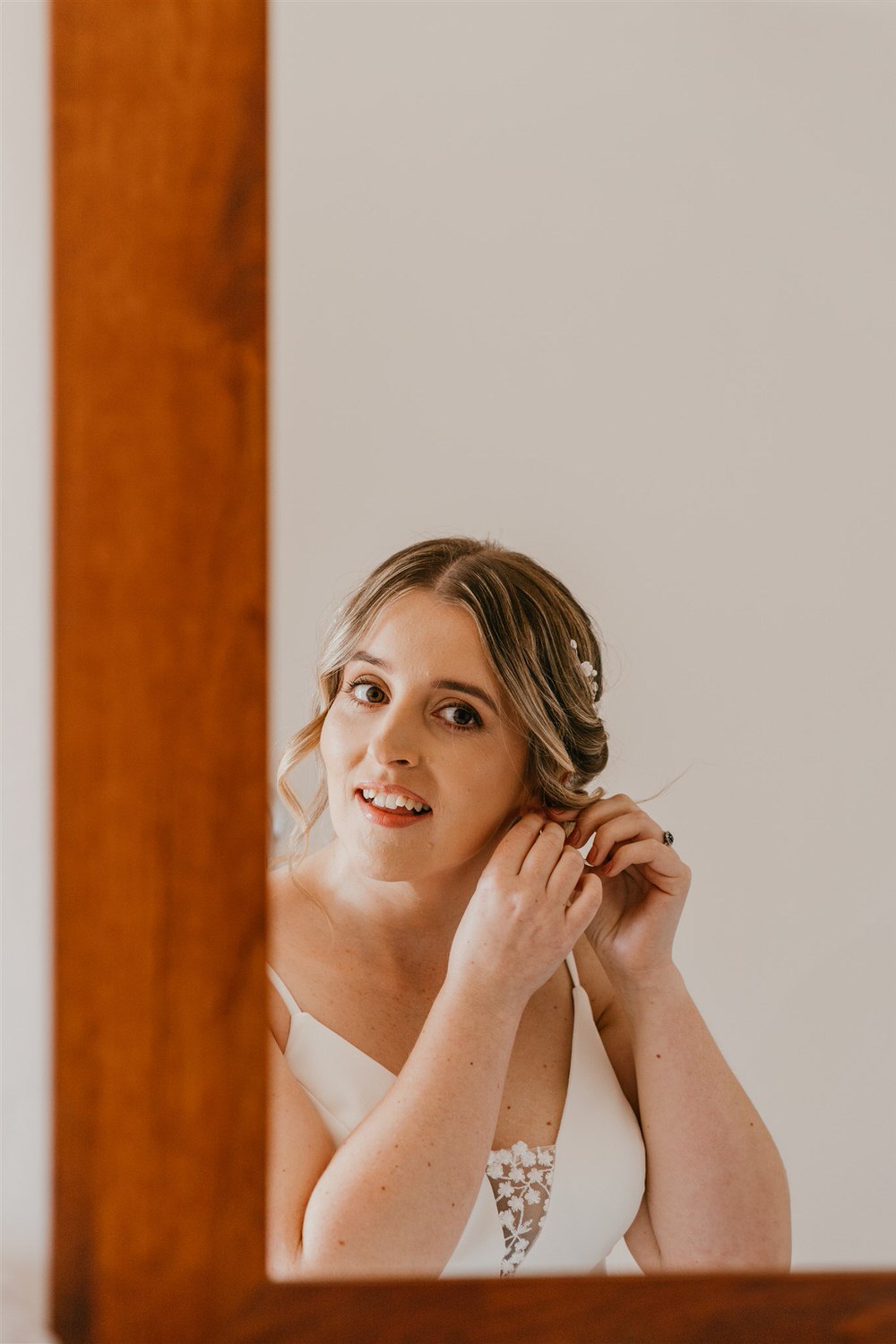 bride putting in her earrings in mirror