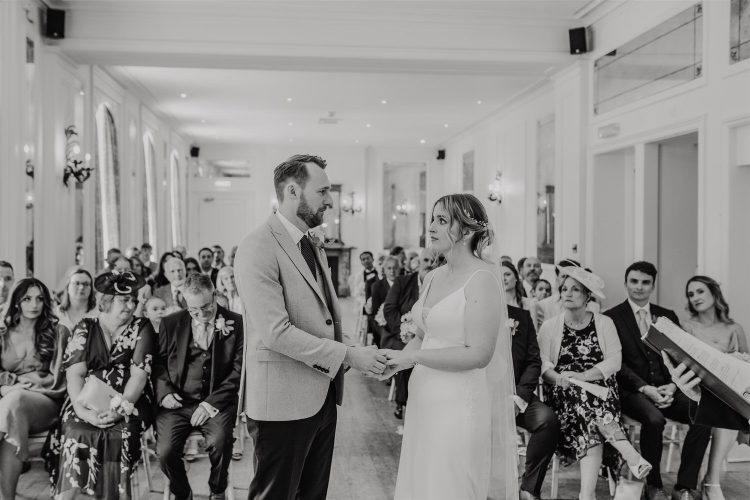 black and white photo of bride and groom exchange rings during wedding ceremony at hotel du vin tunbridge wells