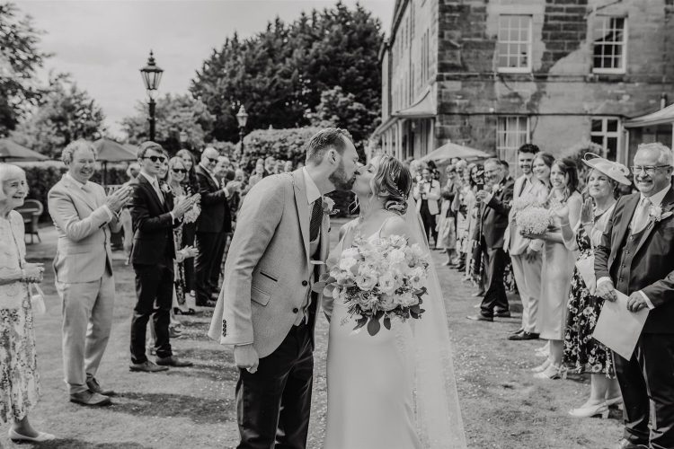 black and white photo of kiss at the end of confetti tunnel in the gardens at hotel du vin tunbridge wells