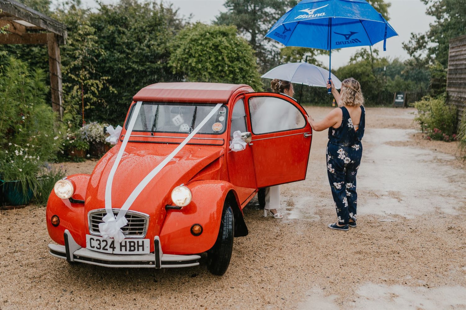 bride arrives in the rain with red vintage wedding car