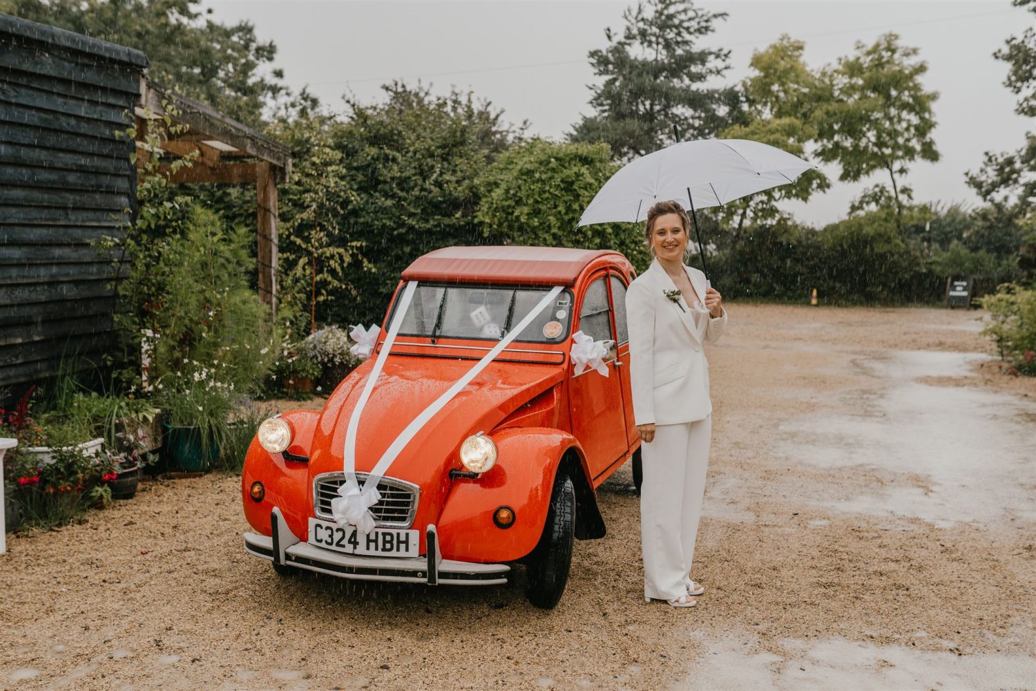 bride poses in the rain with red vintage wedding car