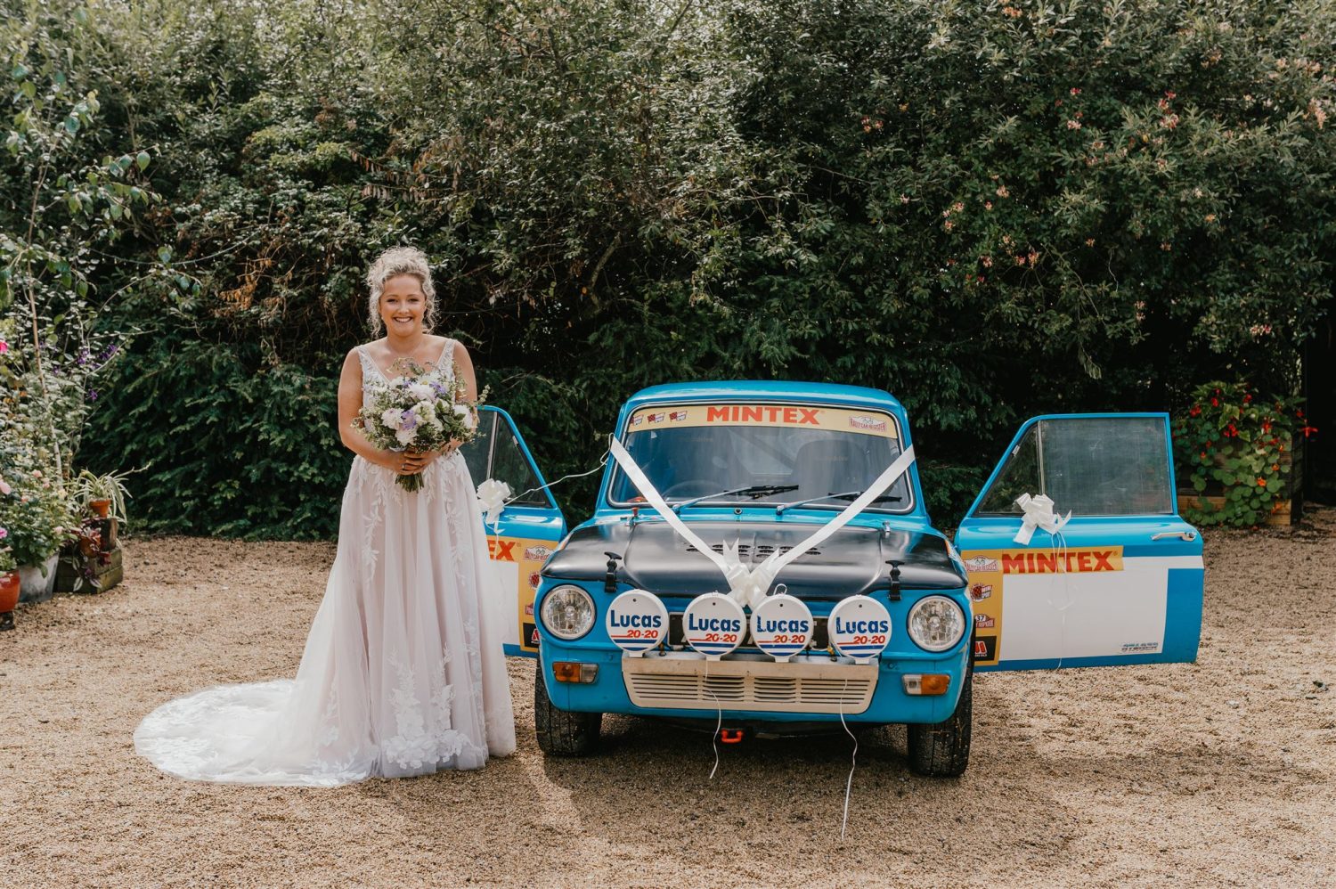 bride poses with rally car at acorn barn wedding ceremony