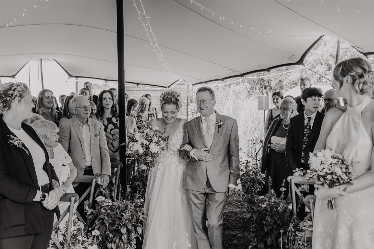black and white photo as bride walks down the aisle with father at acorn barn wedding ceremony