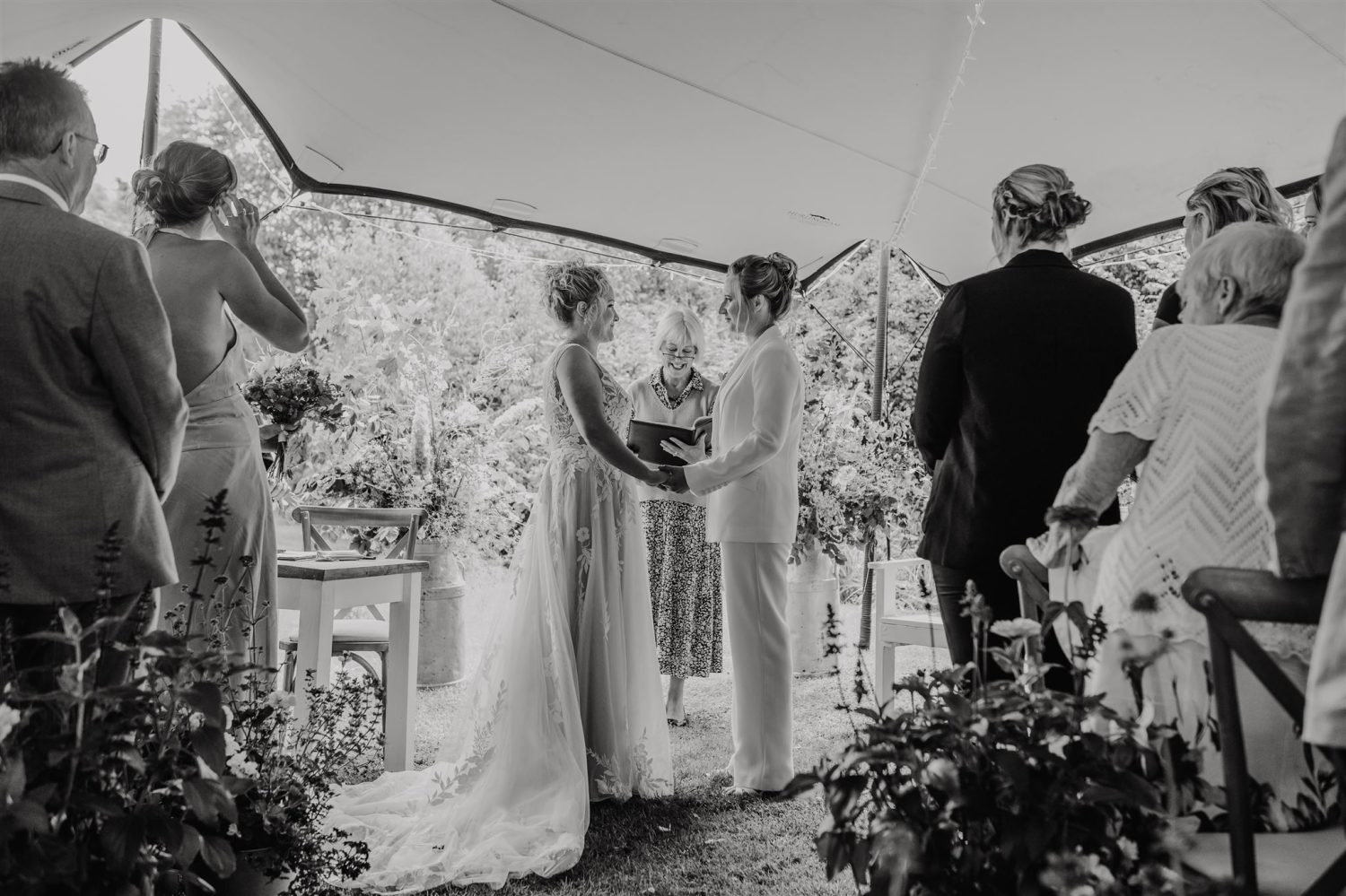 black and white photo of brides saying their vows to each other during garden ceremony at acorn barn wedding venue in oxfordshire