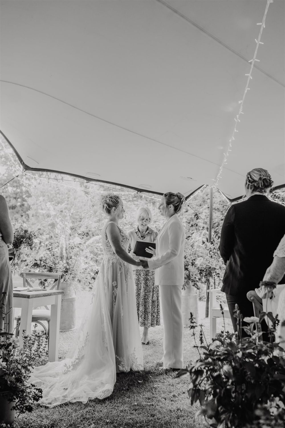 black and white photo of brides saying their vows to each other during garden ceremony at acorn barn wedding venue in oxfordshire