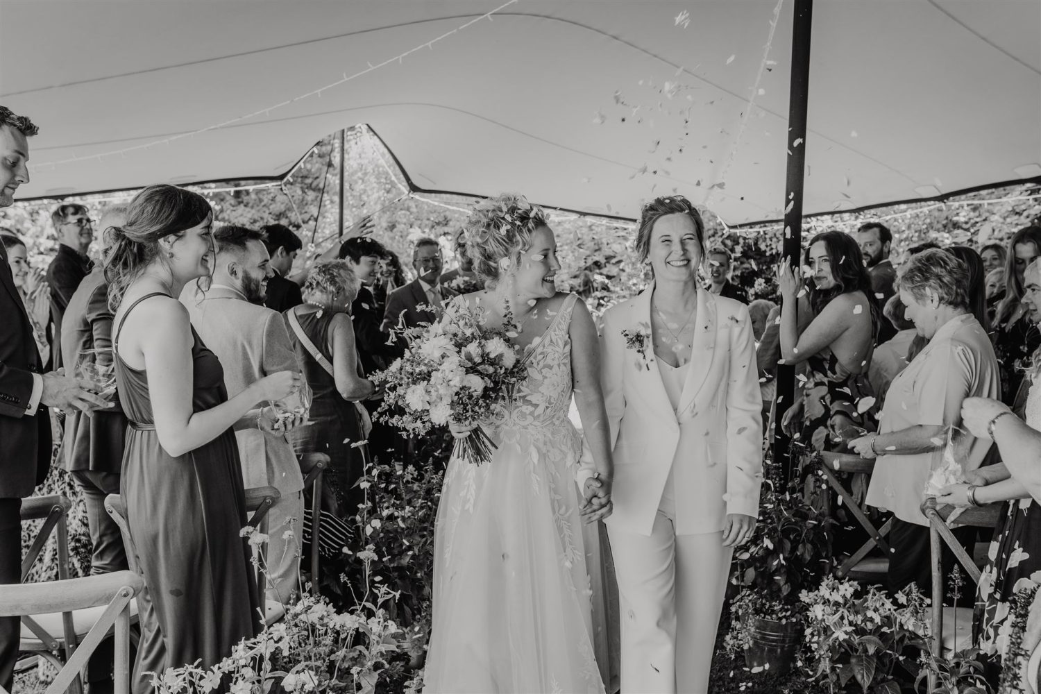 black and white photo of brides whilst their wedding guests throw confetti as they walk back up the aisle of garden wedding ceremony