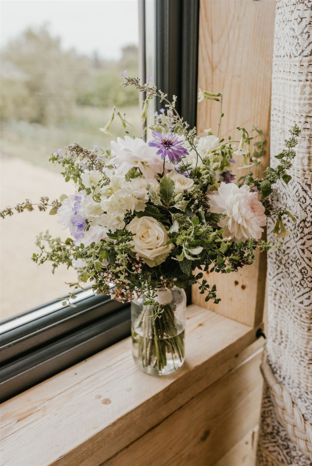 bridal bouquet of green, white and purple in a vase on a windowsill