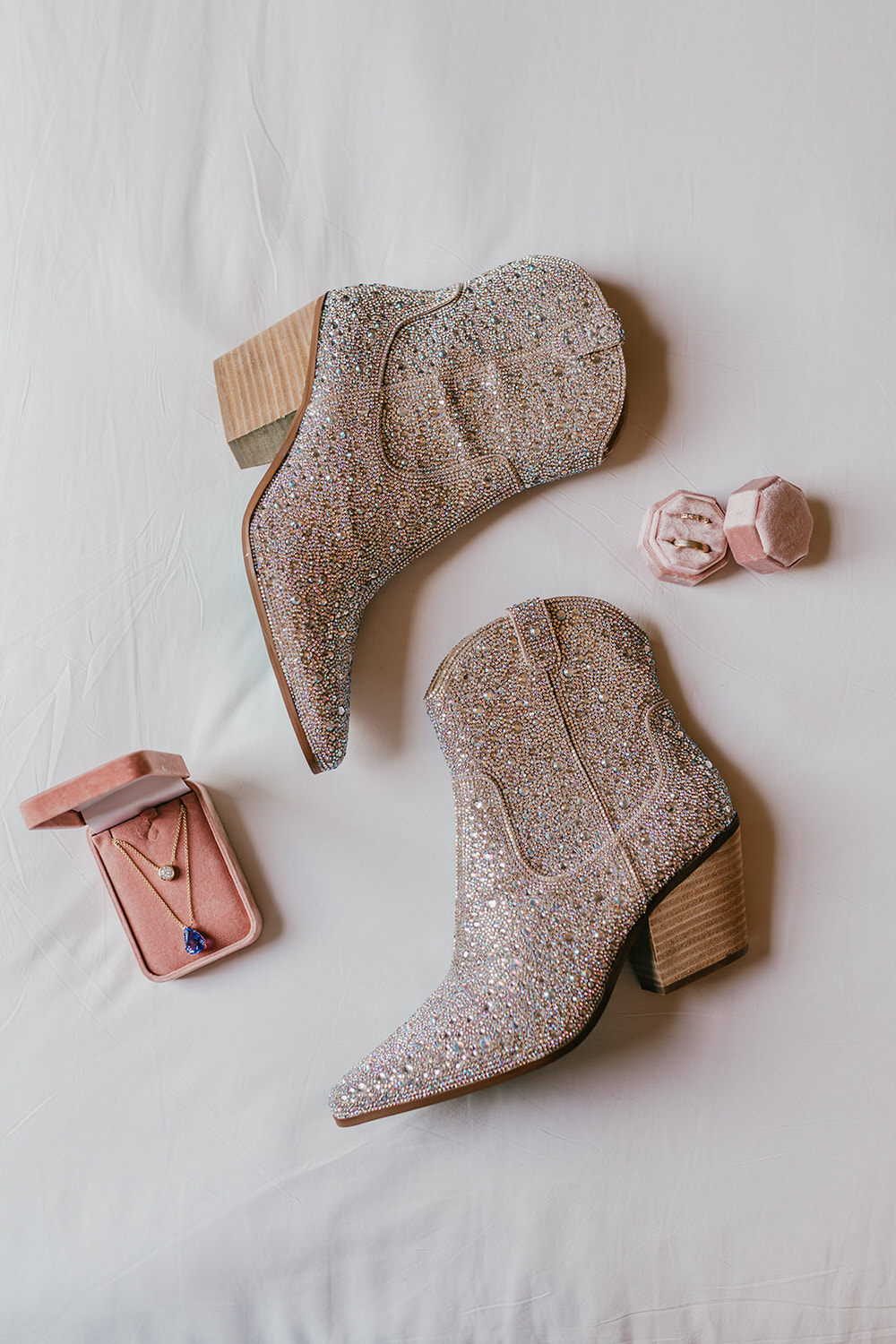 sparkly cowgirl boots sitting on the bed with rings and necklace in pink boxes in morden hall bridal prep suite