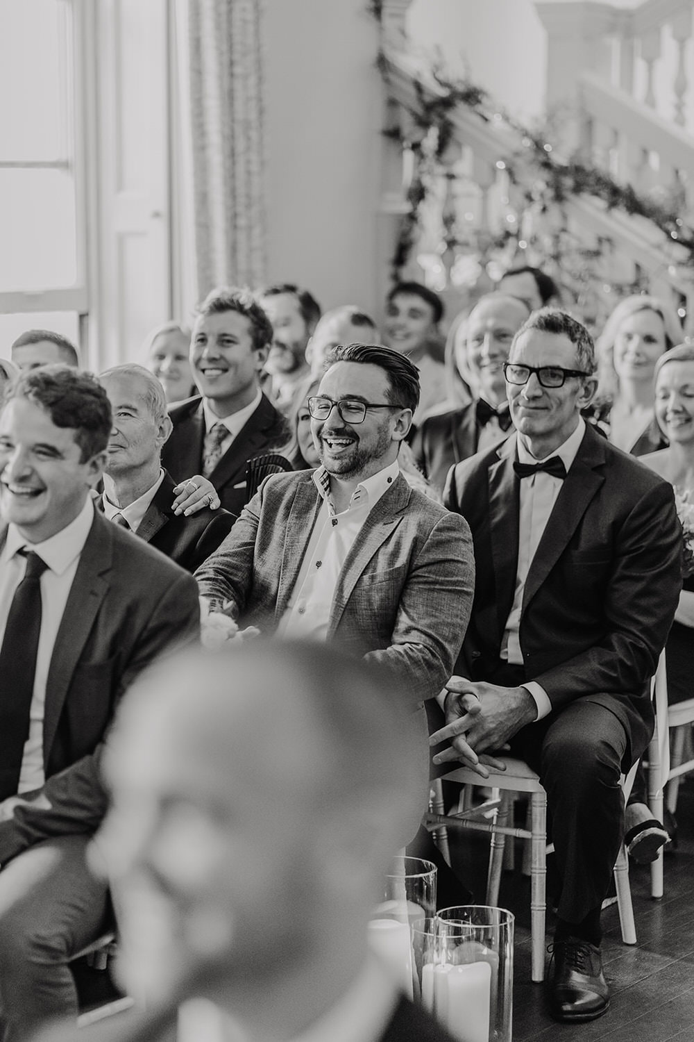 black and white photo of wedding guest laughing during wedding ceremony at morden hall in london