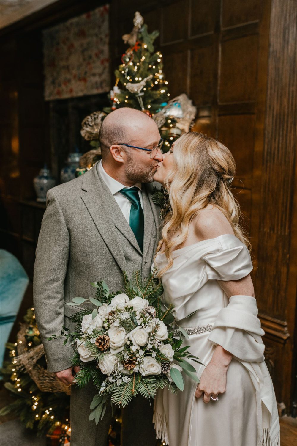 bride and groom kiss in front of a christmas tree at winter wedding in surrey