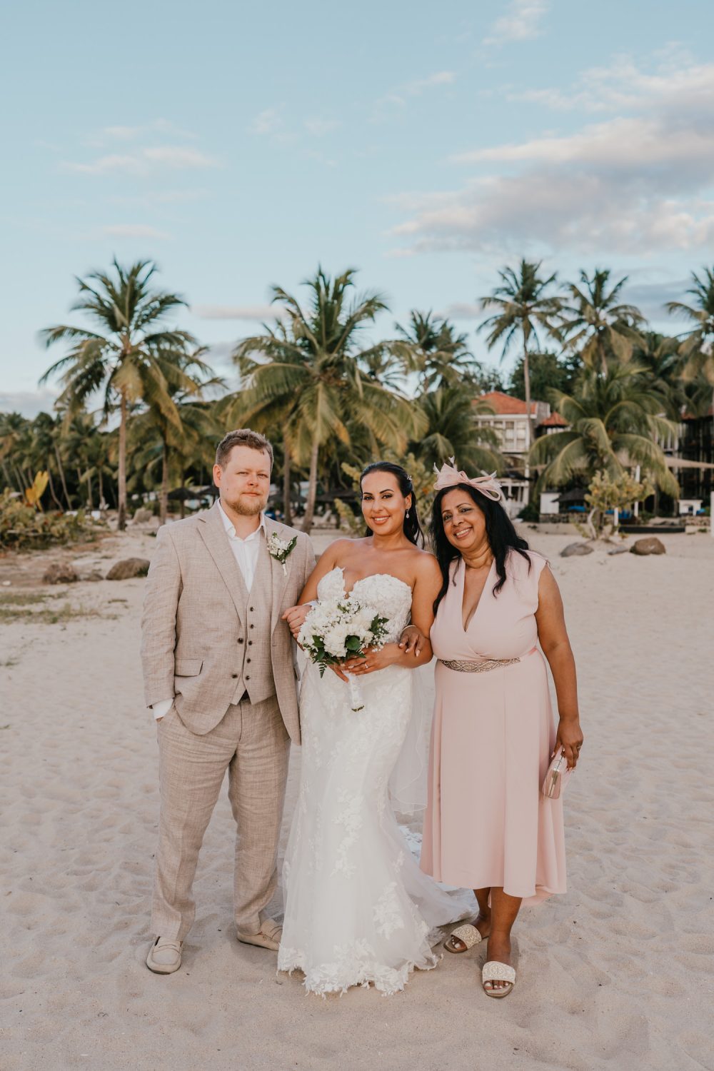 bride and groom stand together with bride's mum on the beach at stolentime resort saint lucia wedding venue