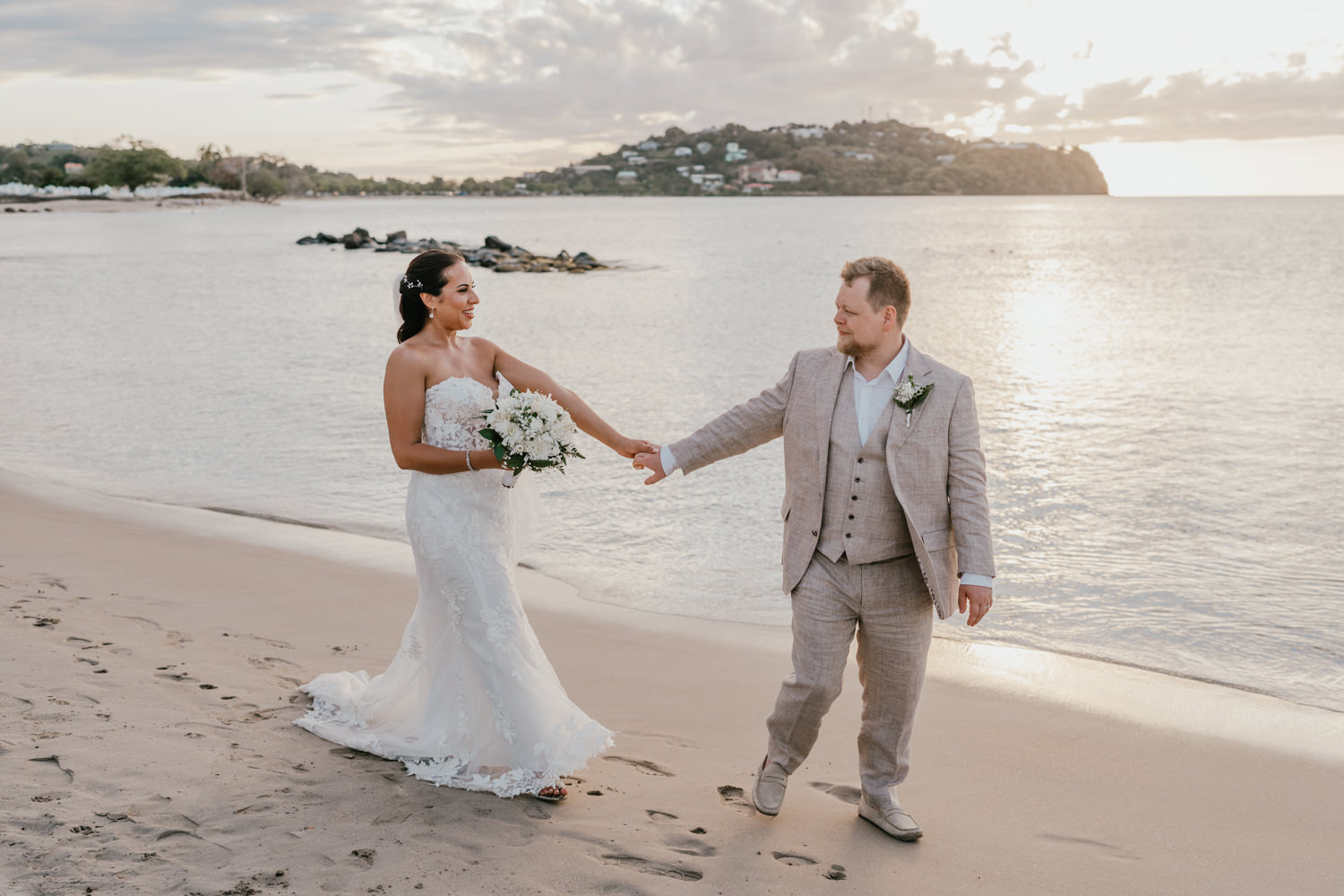 bride and groom stroll hand in hand on the beach in saint lucia at sunset for golden hour couple portraits during their caribbean wedding