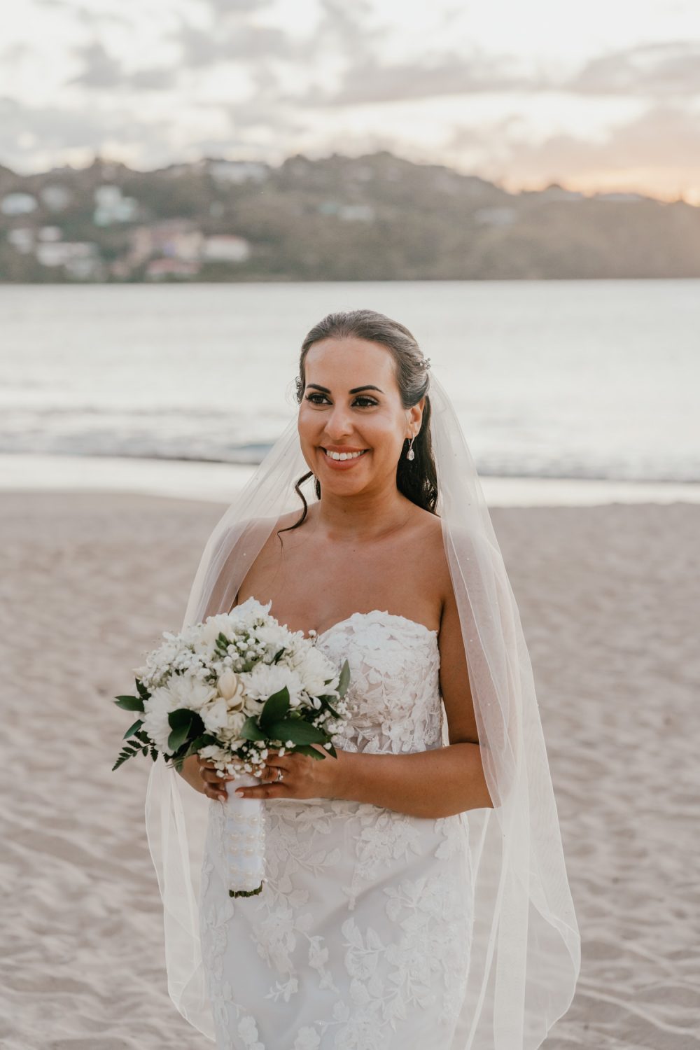 groom stands on the beach in saint lucia holding bouquet