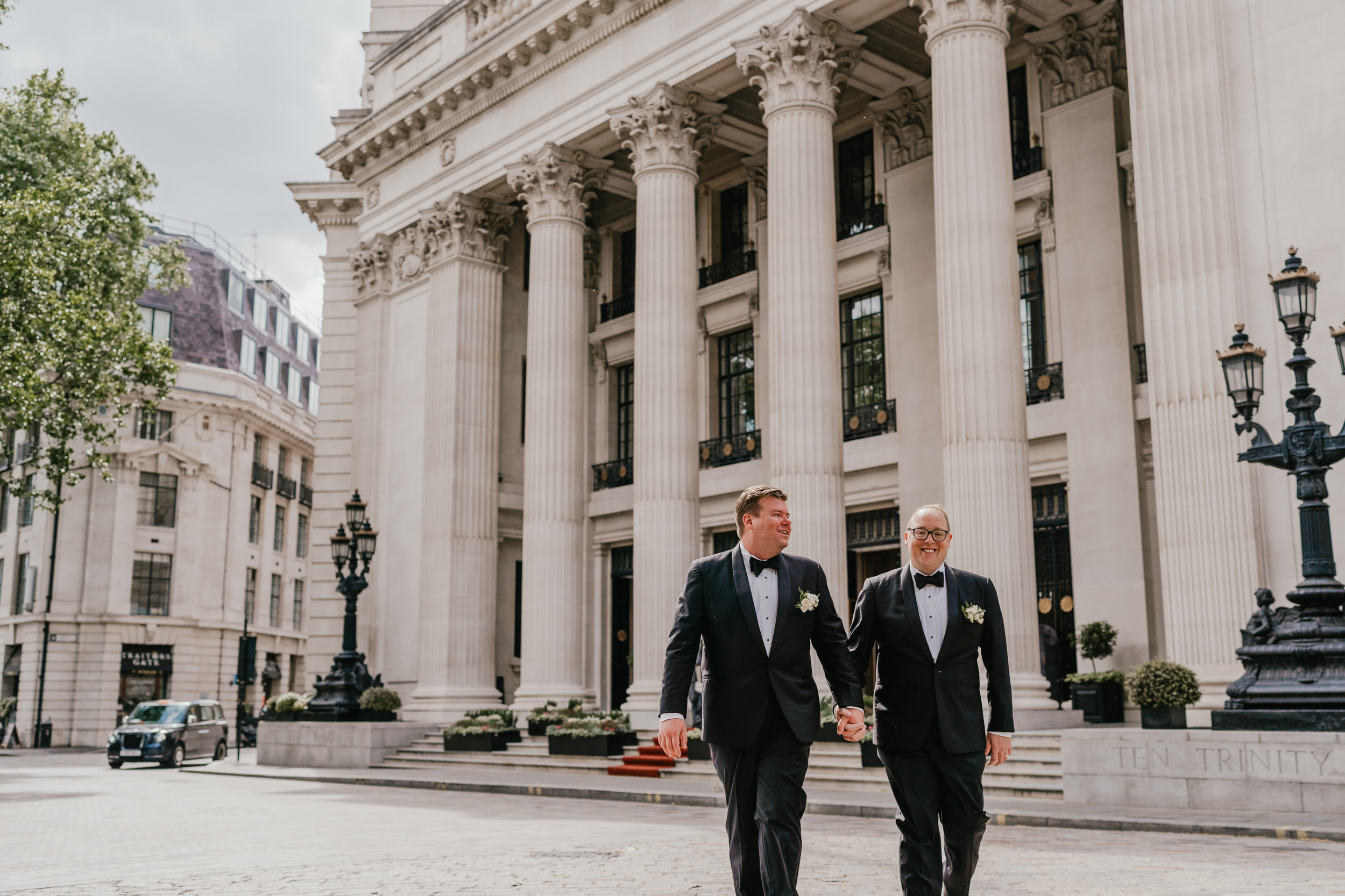two grooms walking hand in hand in front of the four seasons hotel in tower hill