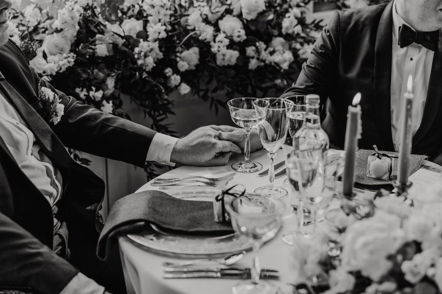 black and white photo of grooms holding hands during speeches in the library at trinity house wedding venue in london