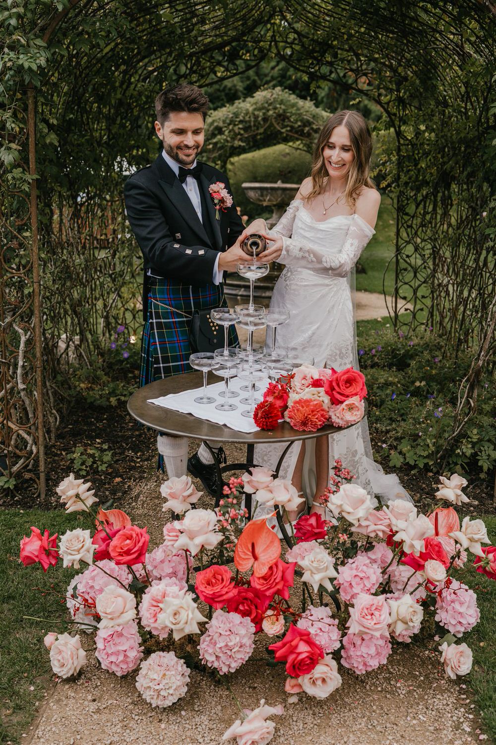 bride and groom do champagne tower surrounded by pink flowers at the beacon tunbridge wells wedding