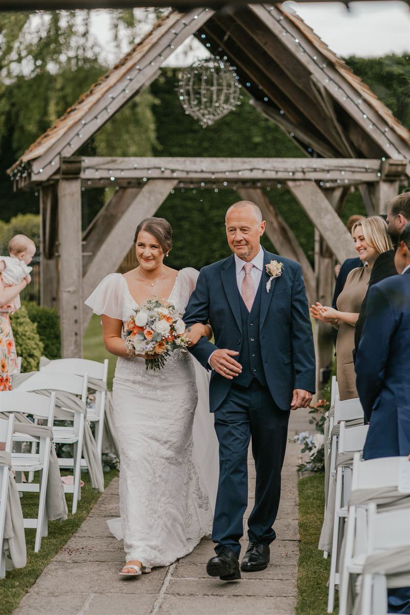 bride walks down the aisle with her father at outdoor winters barns wedding