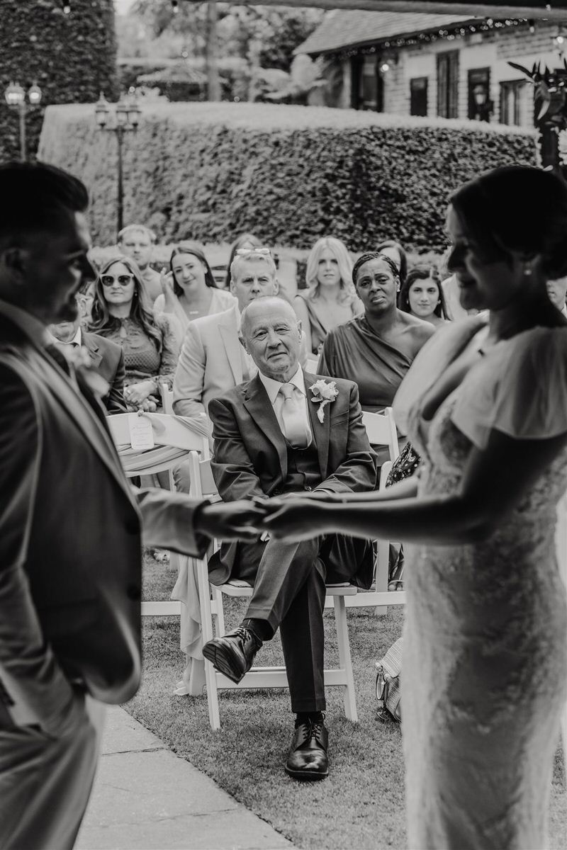 black and white image of father of the bride watching as couple exchange rings during wedding ceremony at winters barns