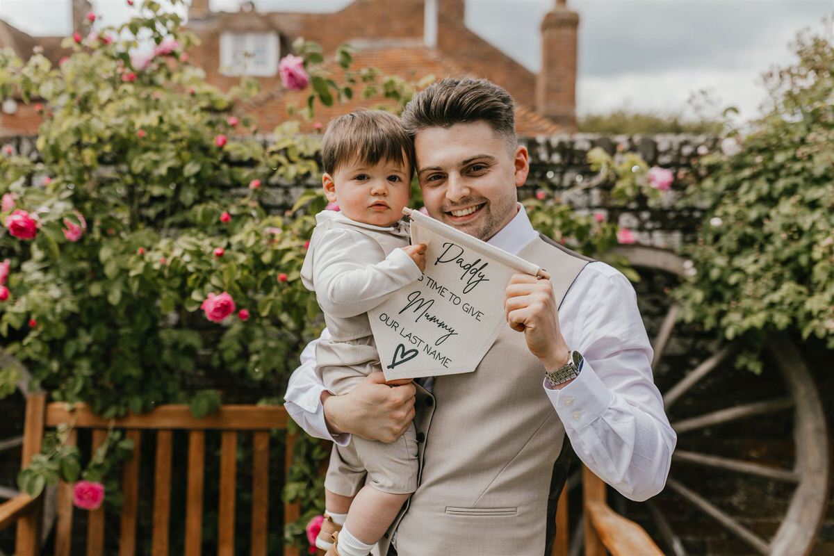 groom and his baby holding a wedding sign at winters barns wedding in canterbury